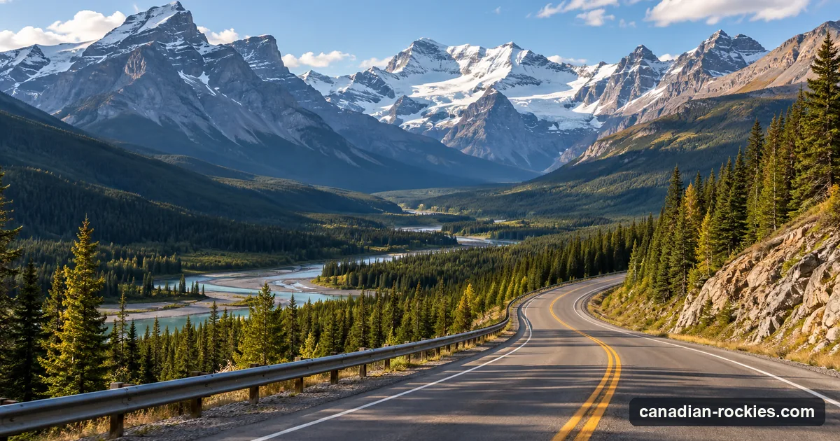 An empty mountain highway curving through a forested valley below glaciated peaks